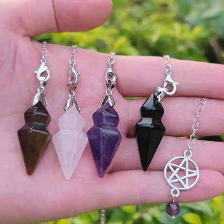 Four crystal pendulums on chains held in a hand with a blurred green background