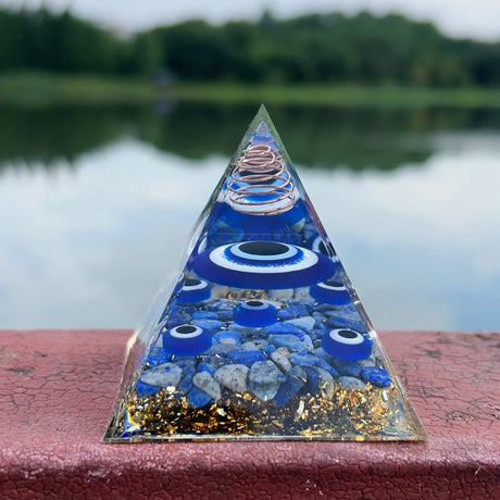 Pyramid-shaped object with blue and gold elements on a red surface with a blurred natural background