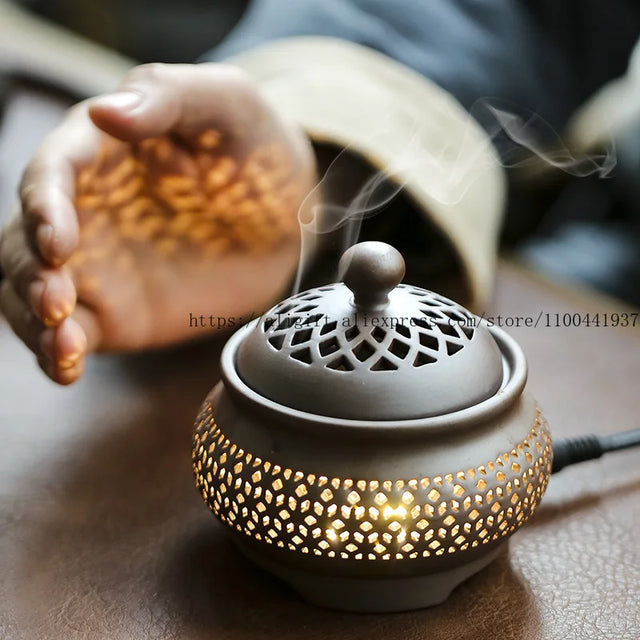 Ceramic incense burner with smoke on a wooden surface, blurred hands in the background.