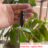 Hand holding a pendant with beads against a green leafy background