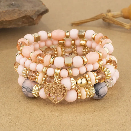 Stack of pink and gold beaded bracelets with a heart charm on a beige surface.