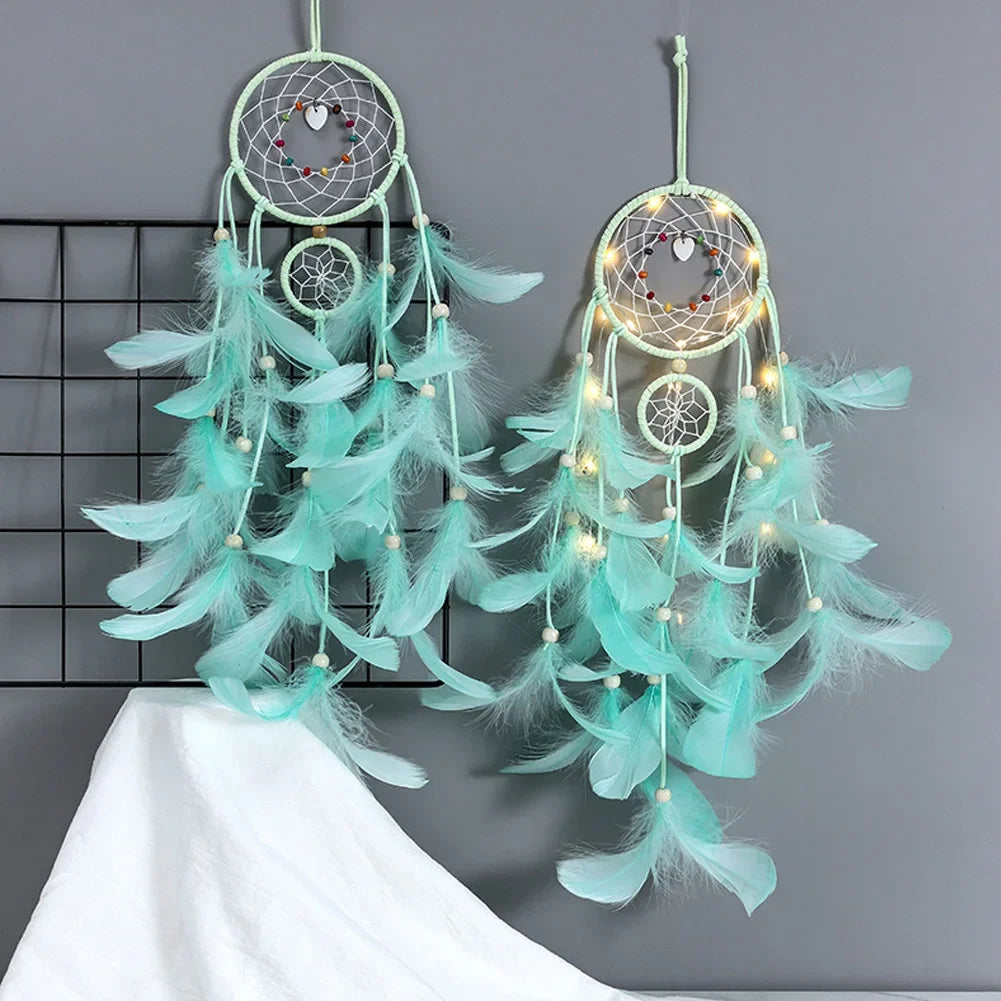 Two turquoise dreamcatchers with feathers and lights on a gray background