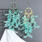 Two turquoise dreamcatchers with feathers and lights on a gray background