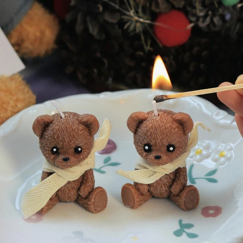 Two small teddy bear figurines with scarves on a white plate, one being lit by a match.