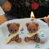 Two small teddy bear figurines with scarves on a white plate, one being lit by a match.