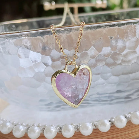 Heart-shaped pink stone necklace with gold chain on a decorative stand.