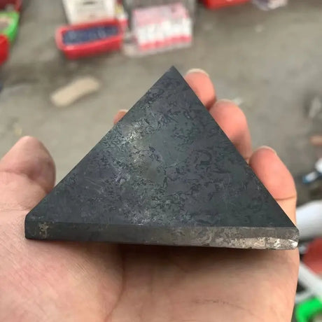 Triangular black stone held in a hand with a blurred background