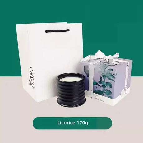 Black candle with packaging and a gift bag on a white surface with a green background
