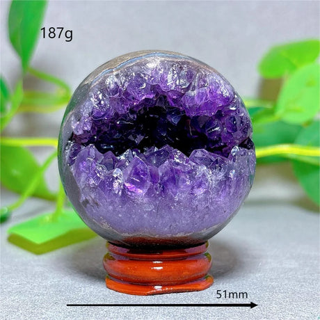 Amethyst crystal sphere on a stand with green leaves in the background