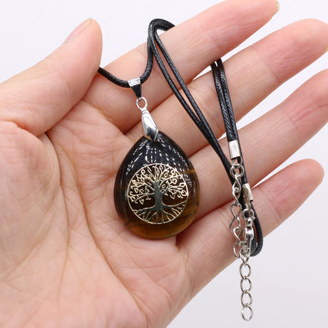 Hand holding a necklace with a tree-of-life pendant on a white background