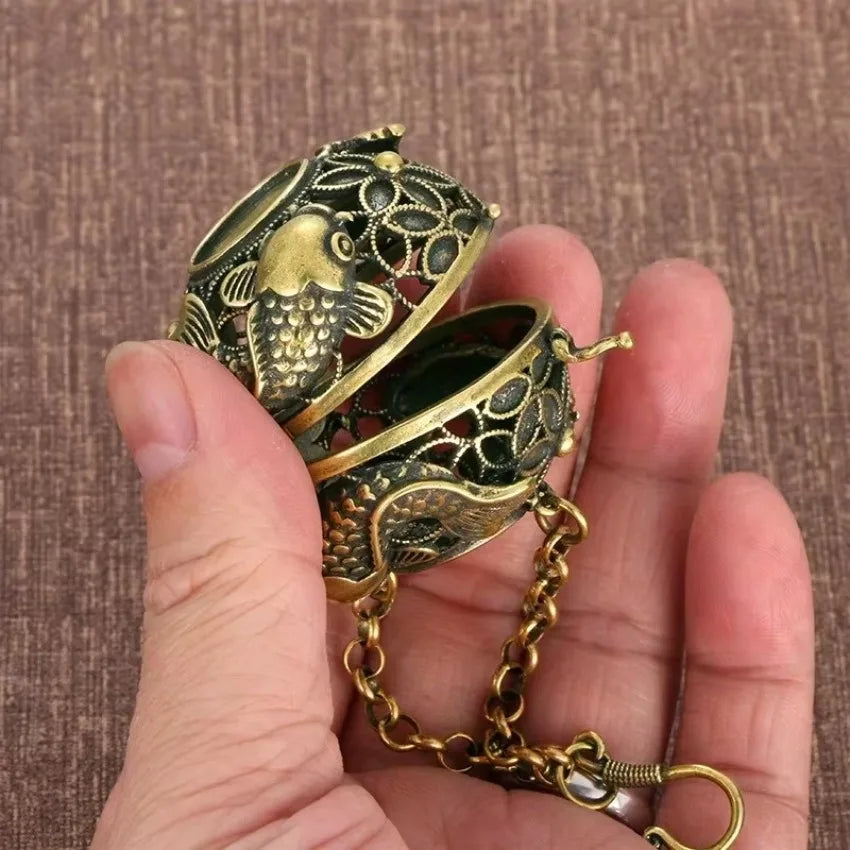 Decorative brass box with intricate designs held in a hand against a brown background