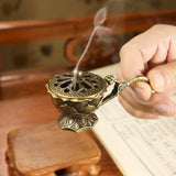 Bronze incense burner with a hand holding it, set against a wooden background.