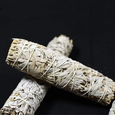 Two bundles of sage wrapped in twine on a black background