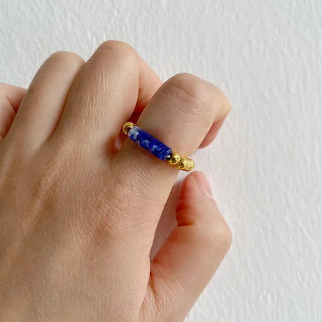 Hand wearing a ring with blue stone and gold band on a plain background