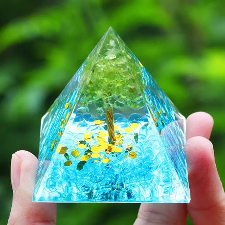 Pyramid-shaped crystal with blue liquid and yellow stones held by a hand against a green blurred background