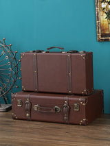 Two brown suitcases stacked on a wooden surface with a teal wall in the background.