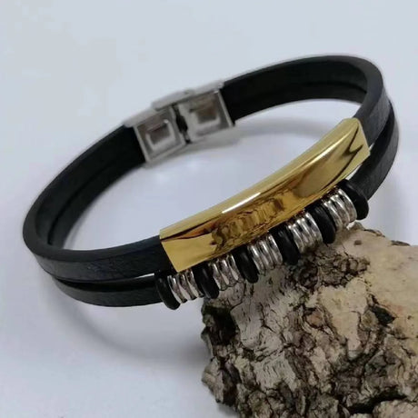 Black leather bracelet with gold and silver accents on a white background