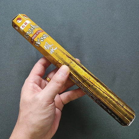 Hand holding a yellow box of incense sticks against a gray background