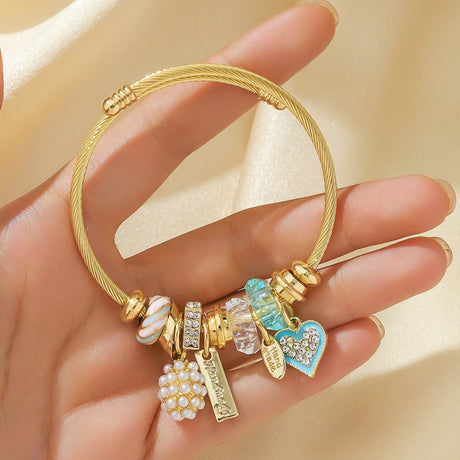 Gold bracelet with various charms held in a hand against a beige background