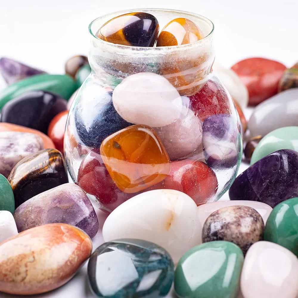 Glass jar filled with multicolored marbles surrounded by various stones on a white background