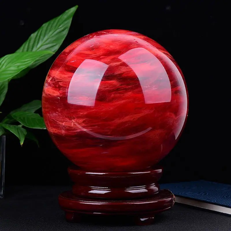 Red crystal ball on a wooden stand with green leaves in the background