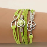 Green braided bracelet with silver heart and arrow charms on a wrist.