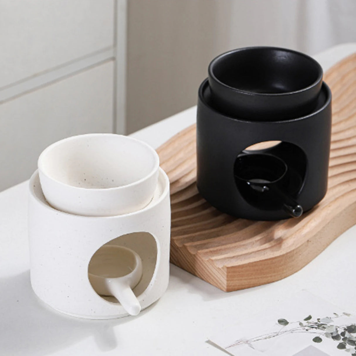 Two ceramic diffusers, one white and one black, on a wooden tray.