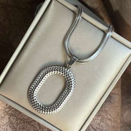 Silver necklace with a textured pendant on a light gray box