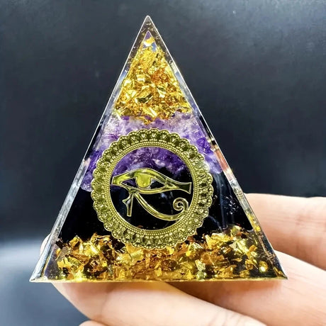 Triangular crystal pyramid with eye symbol held by a hand against a dark background