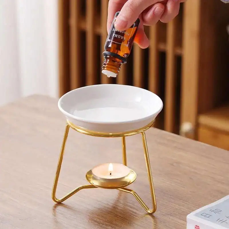 Person pouring essential oil into a white dish with a candle on a wooden surface