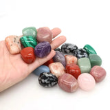 Hand holding a collection of multicolored tumbled stones on a white background