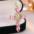 Gold cross necklace with pink gemstones on a blurred background