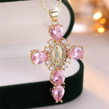 Gold cross necklace with pink gemstones on a blurred background