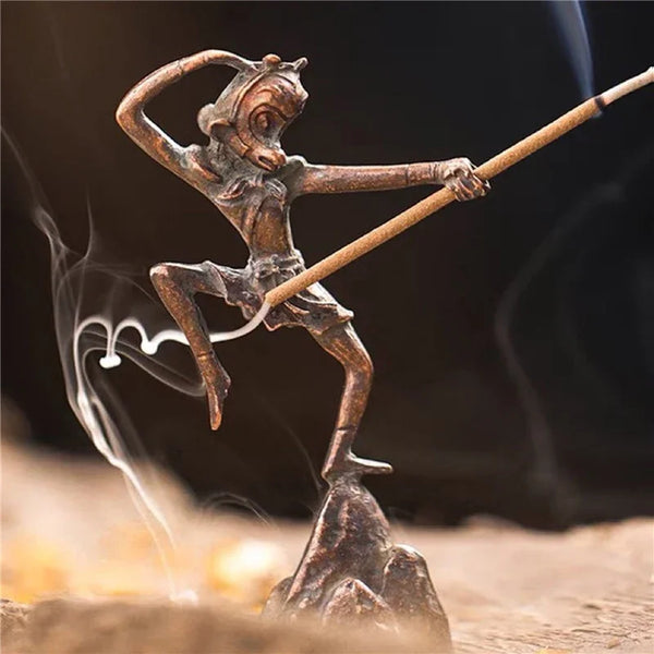 Bronze sculpture of a figure on a rock with a staff, surrounded by smoke.