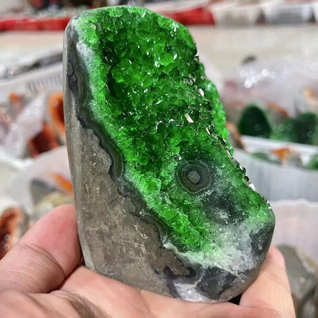 Green crystal rock held in a hand with a blurred background