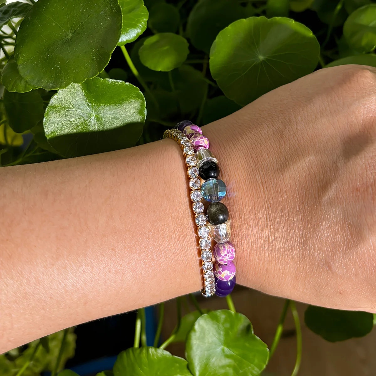 Close-up of a wrist wearing two beaded bracelets with a green leafy background