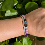 Close-up of a wrist wearing two beaded bracelets with a green leafy background