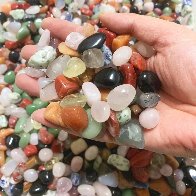 Hand holding a variety of multicolored stones with a background of more stones.