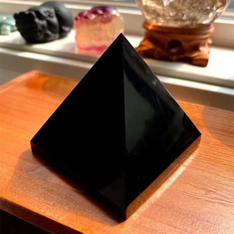 Black pyramid crystal on a wooden surface with blurred background