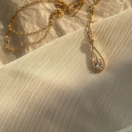 Gold necklace with a teardrop-shaped pendant on a beige fabric background