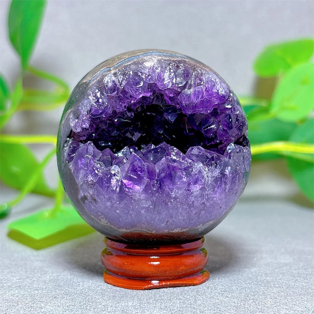 Amethyst crystal sphere on a stand with green leaves in the background