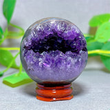 Amethyst crystal sphere on a stand with green leaves in the background