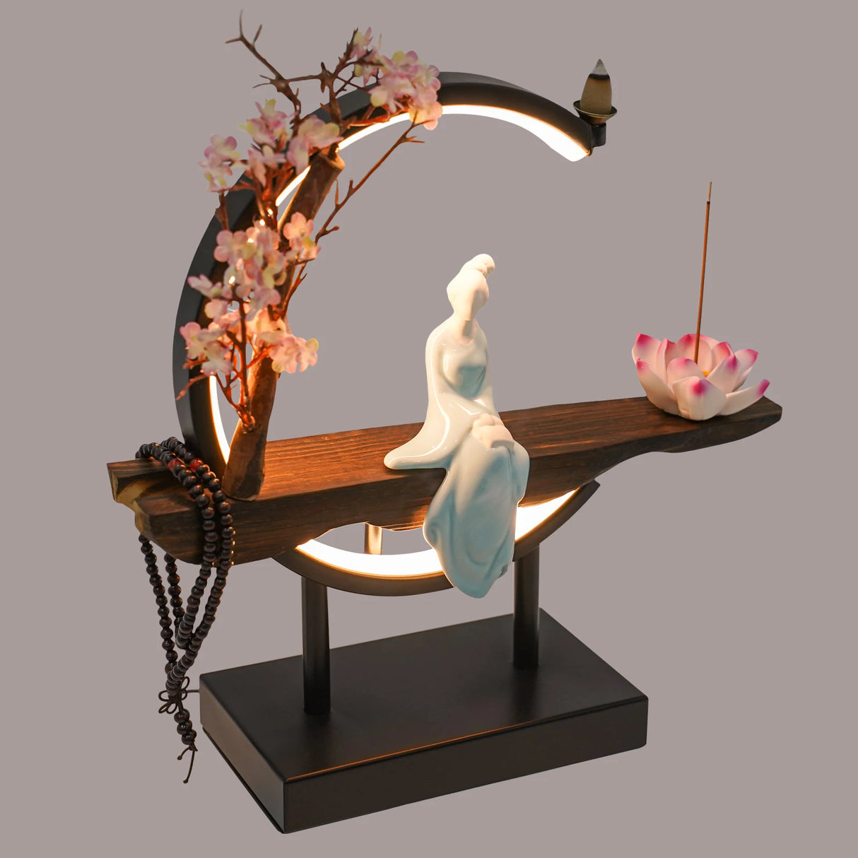 Decorative lamp with a sitting figure, flowers, and incense on a gray background