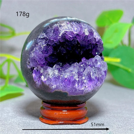 Amethyst geode crystal on a stand with green leaves in the background