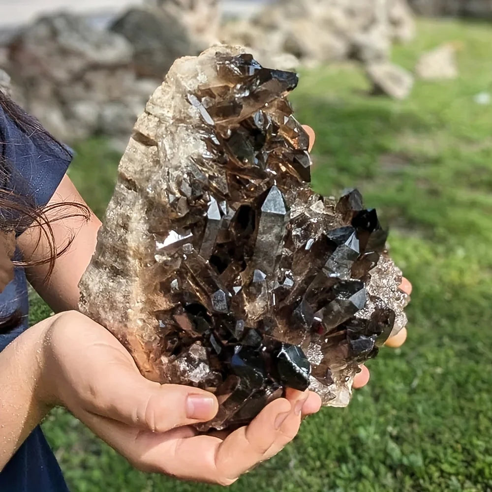 Person holding a large crystal cluster outdoors with grass in the background