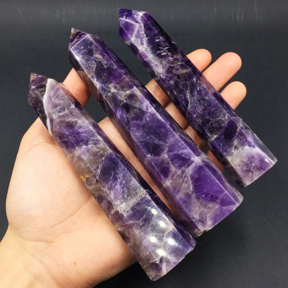 Hand holding three purple amethyst crystal sticks against a dark background