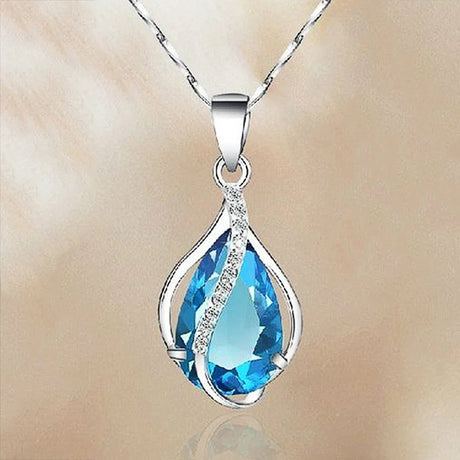 Silver pendant with a blue teardrop-shaped gemstone on a beige background