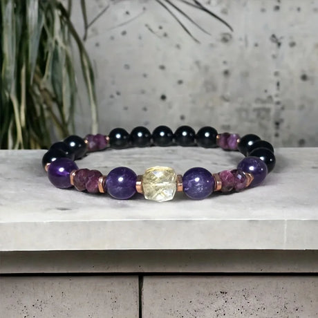 Beaded bracelet with purple, black, and rose gold beads on a concrete surface.