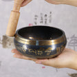 Tibetan singing bowl with a wooden striker held by hands against a light background