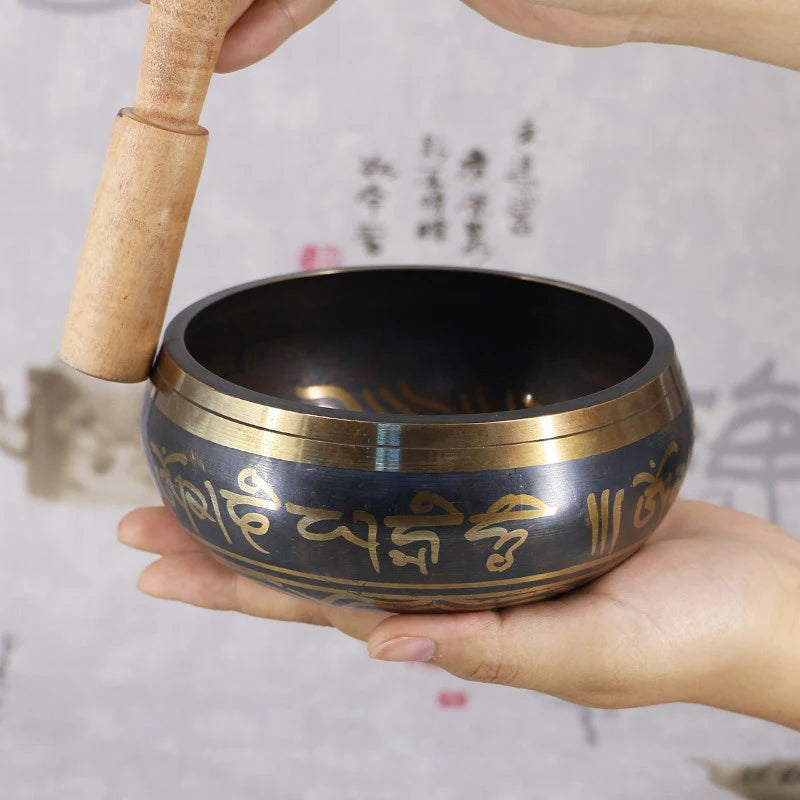 Tibetan singing bowl with a wooden striker held by hands against a light background